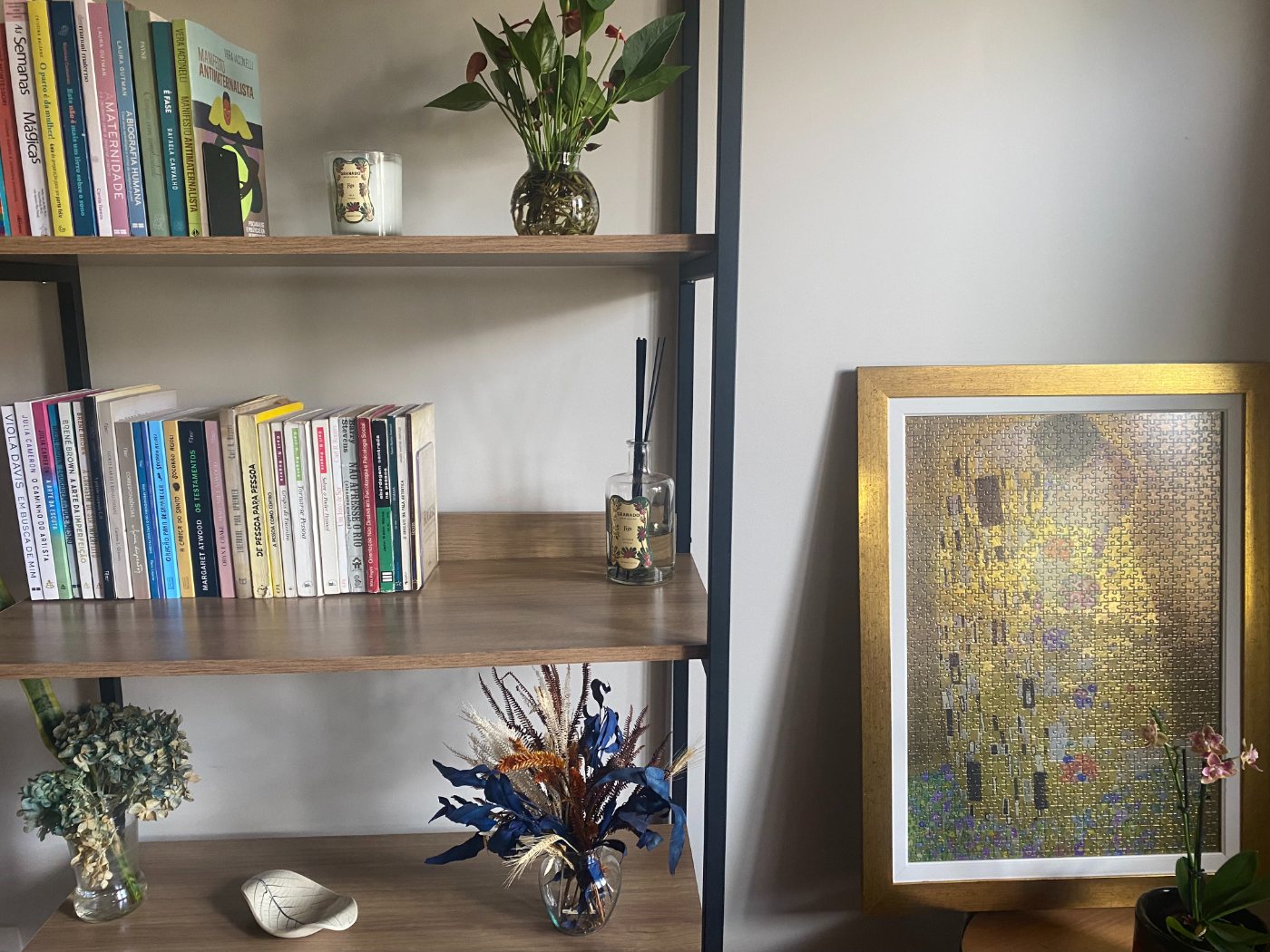 Estante do consultório com livros, flores secas e um quebra-cabeça montado de O Beijo, de Klimt